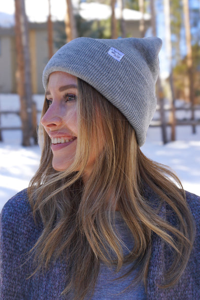 Picture of a woman with a Solid Knit Beanie on in the light heather grey color