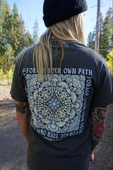 Person wearing a black t-shirt with a white mandala design and text outdoors.