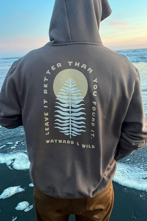 Person wearing a hoodie with a nature-themed design by a body of water.