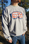 Person wearing a gray sweatshirt with a colorful logo outdoors