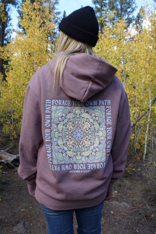 Person wearing a hoodie with a design and text in a forest setting