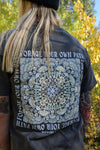 Person wearing a black t-shirt with a design and text in a forest setting
