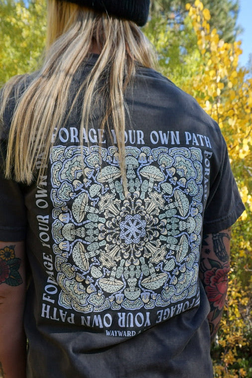 Person wearing a black t-shirt with a design and text in a forest setting