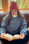 Person wearing a blue sweatshirt that says "just one more chapter" while reading a book indoors.