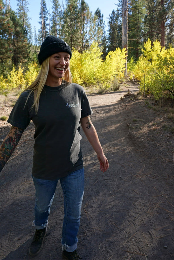 Person standing on a dirt path in a forest with trees and bushes in the background