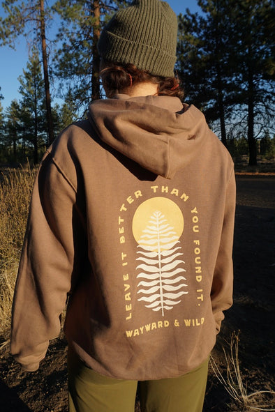 Person wearing a brown hoodie with a tree design and text in a forest setting