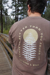 Person wearing a brown t-shirt with a leaf design and text in a forest setting