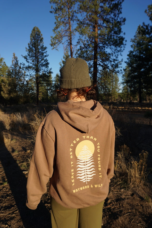 Person wearing a brown hoodie with a logo and text in a forest setting
