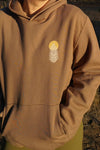 Brown hoodie with a logo on the chest against a natural background