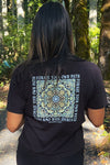 Person wearing a black t-shirt with a design and text in a forest setting