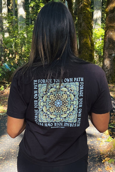 Person wearing a black t-shirt with a design and text in a forest setting