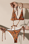 Bikini set with orange red and green pattern of oranges held by hands against a beige background