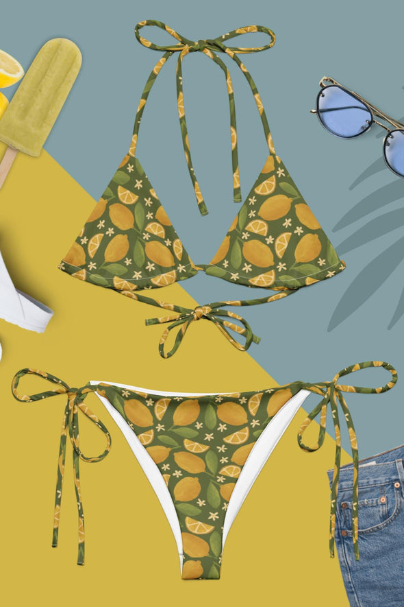 Green bikini set with lemon pattern on a yellow and blue background with sunglasses and lemon slices.