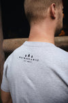 Photo of a guy wearing the light gray TREES COFFEE BEER T-Shirt showing the Wayard & Wild and three little pine tree logo on the back. He standing in front of a lodge at Silver Falls State Park in Oregon.