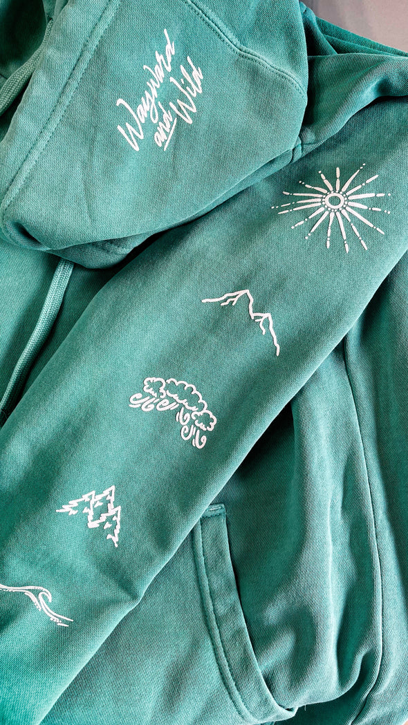 Picture showing close up hood and sleeve print of the pigment wash mint Elements Hoodies. Hood print says Wayward & Wild in a script font and the sleeve prints are hand drawn symbols of fire, earth, air and wind.