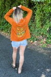 Kolbi wearing an orange zip hoodie with a mushroom design on the back that says Take a Trip at the bottom