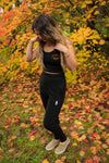 Full body photo of woman wearing the black pine joggers looking down at her feet with fall leaves in the background