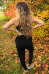 Full body photo of the back of a woman wearing black joggers looking into the distance with fall leaves in the background