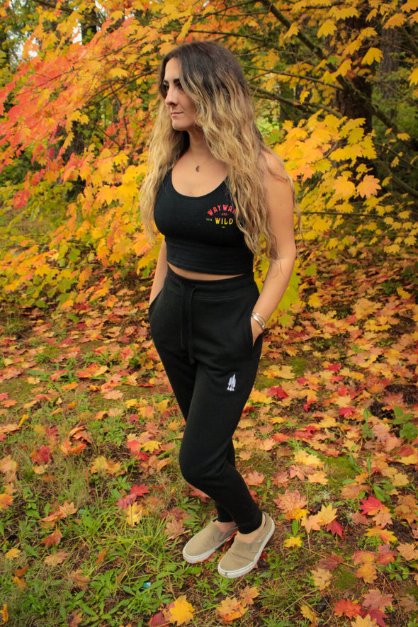 Full body photo of woman wearing black joggers looking into the distance with fall leaves in the background