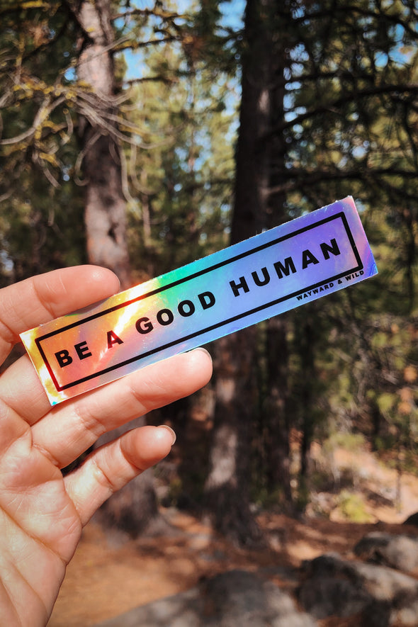 Photo of the rectangular holographic sticker that says "Be A Good Human"