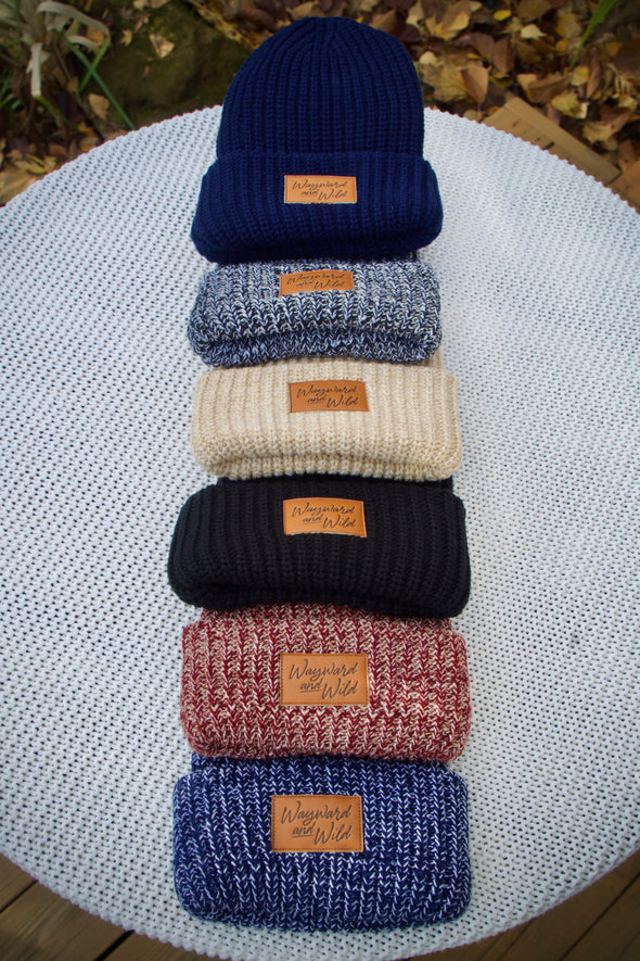 Flat lay of all the colors of the Chunky Knit Beanies. Photo shows the light gray and white, black, navy blue, Salt and pepper, dark gray, maroon and white, navy and white and tan and white colors.
