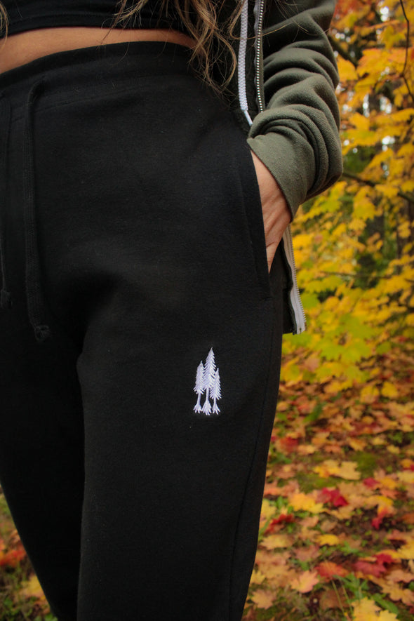 close up detail photo of Kolbi in the black joggers showing the detail of the three trees embroidered near the pocket with hand in pocket