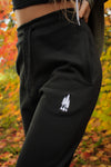 close up detail photo of Kolbi in the black joggers showing the detail of the three trees embroidered near the pocket